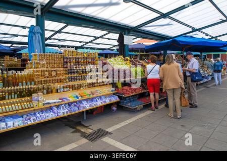 Turisti che navigano in un mercato all'aperto pieno di miele, olio d'oliva, lavanda e frutta fresca sotto una struttura con tetto in metallo in Croazia, Europa Foto Stock