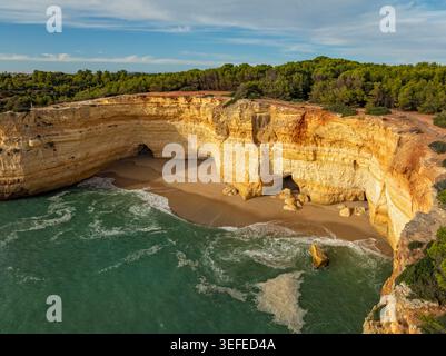 Vista delle scogliere sopra la grotta di Benagil nell'Algarve, Portogallo, con una baia sabbiosa, pareti di roccia calcarea, onde atlantiche e acqua turchese. Foto Stock