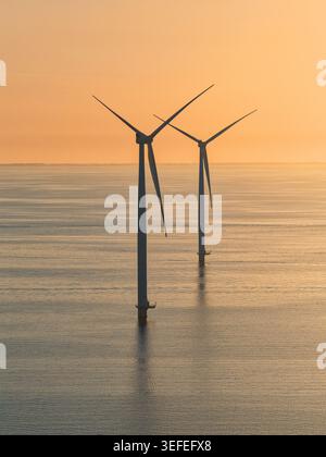 Vista aerea di due turbine eoliche offshore in piedi nel mare calmo sotto un cielo dorato al tramonto al largo della costa a Noordoostpolder, nei Paesi Bassi. Foto Stock
