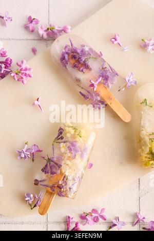 Tavola con bellissimi popsicles floreali e fiori di lilla su sfondo piastrelle chiaro Foto Stock