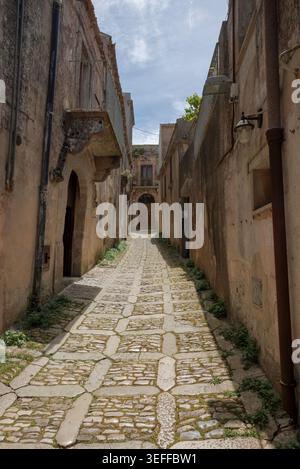 Un tranquillo vicolo acciottolato si snoda attraverso l'antico villaggio collinare di Erice, in Sicilia, fiancheggiato da mura rustiche in pietra Foto Stock