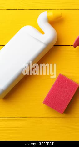 Materiali di pulizia su una superficie gialla con una spugna e un flacone Foto Stock