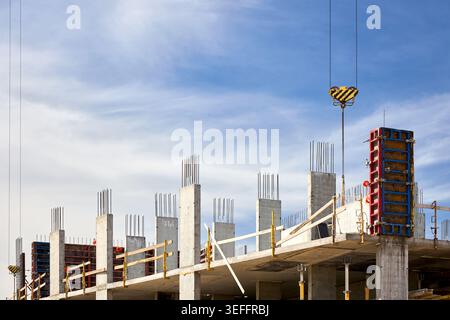 cantiere in corso, con colonne in cemento rinforzate con armature in acciaio, casseforme rosse e gancio per gru sospeso contro un clou luminoso Foto Stock