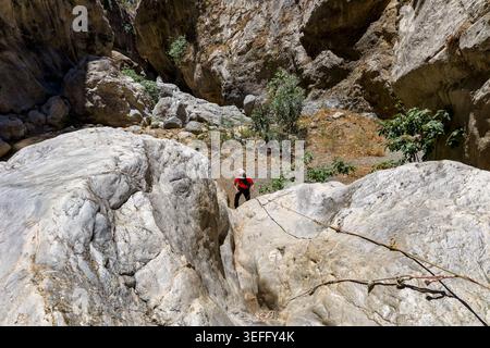 Turista attivo che naviga su terreni rocciosi con corde in una profonda gola del fiume greco Foto Stock