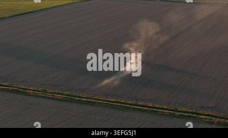 Trattore che coltiva terreno secco nella Pianura Padana al tramonto Foto Stock