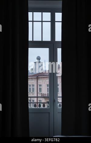 Architettura della città incorniciata da tende viste dall'interno di un appartamento, che mette in risalto il paesaggio urbano, le facciate classiche dell'edificio e l'atmosfera accogliente di Foto Stock