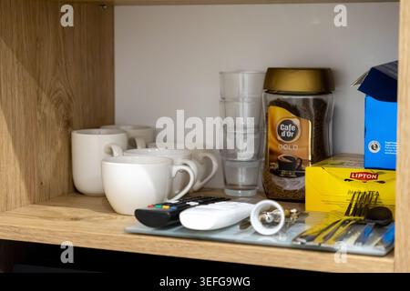 Przemysl, Polonia - 30 marzo 2026: Scatole da tè Lipton e vasetti da caffè Cafe d'Or posizionati sullo scaffale dell'hotel accanto a tazze e telecomandi, che rappresentano il co Foto Stock