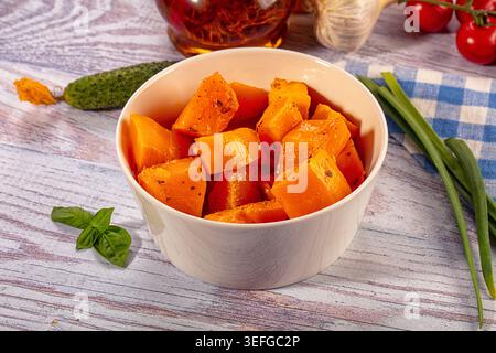 Ciotola di cubetti di zucca arrosto conditi con ingredienti freschi. Piatto vegetariano sano con pomodori, aglio ed erbe su fondo rustico in legno Foto Stock