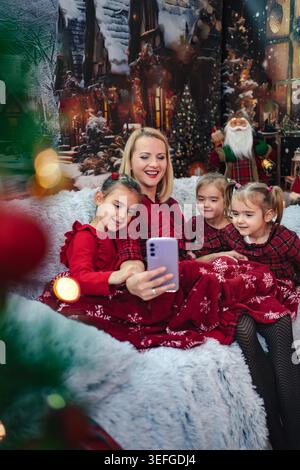 La madre e le sue tre figlie sorridono mentre fanno un selfie festoso su un divano accogliente Foto Stock