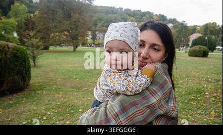 Mamma tiene delicatamente in braccio la bambina di tre mesi in un tranquillo parco verde a Banja Koviljaca, Serbia. La madre tiene in mano delicatamente il suo bambino di tre mesi Foto Stock