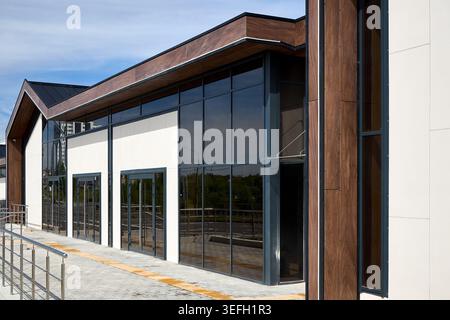 La facciata dell'edificio moderno presenta grandi finestre in vetro, cornici in metallo scuro e pannelli decorativi in legno. Ringhiere in metallo passerella in calcestruzzo sotto il basamento Foto Stock