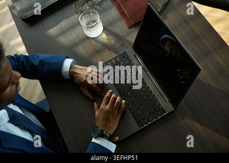 Vista dall'alto dell'uomo d'affari nero che utilizza il laptop alla scrivania, rivedendo il caso di divorzio o i documenti legali in remoto. Ideale per il marketing del diritto di famiglia, la mediazione, la promozione dei servizi legali Foto Stock
