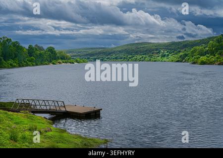 Foto di un tranquillo paesaggio di un fiume tranquillo nel nord del Portogallo sotto le spettacolari nuvole di tempesta, con lussureggianti foreste verdi e un molo tranquillo. Foto Stock