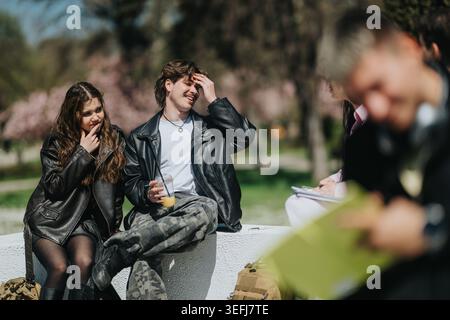 Gli amici della scuola ridono e chiacchierano all'aperto su una parete del campus con giacche in pelle casual Foto Stock