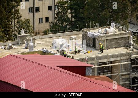 Batumi, Georgia - 26 aprile 2026: Il personale addetto alla costruzione di cappelli rigidi e gilet esegue tetti e muratura sul tetto di un nuovo edificio con impalcature. Foto Stock