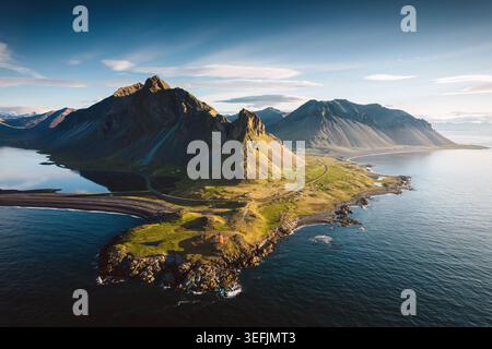 Vista aerea mozzafiato della montagna Eystrahorn che torreggia sulla penisola costiera rocciosa e sul faro durante l'ora d'oro nell'Islanda orientale Foto Stock