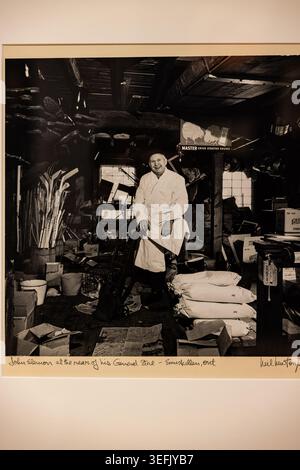 Una fotografia in bianco e nero mostra John Thomson seduto nella stanza posteriore del suo negozio, circondato da utensili, provviste e travi di legno. Foto Stock