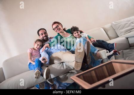Moderna famiglia araba del Medio Oriente che ride insieme sul divano guardando la TV nell'accogliente soggiorno Foto Stock
