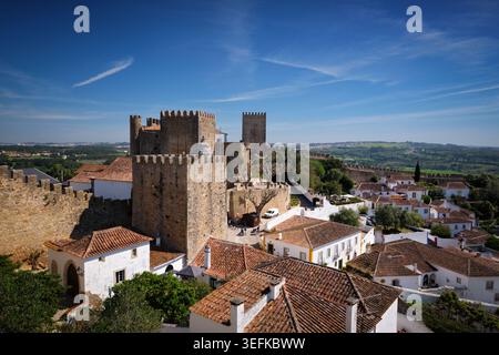 Vista elevata del castello di Obidos a Obidos, Portogallo, con pareti in pietra, tetti piastrellati, case bianche e campagna circostante sotto un cielo blu. Foto Stock
