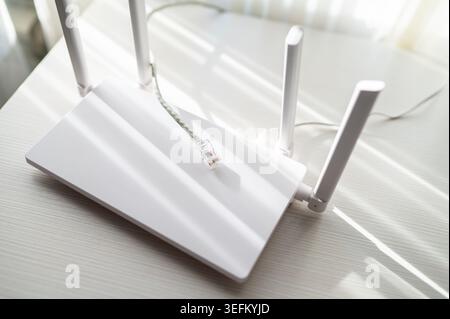 Ripresa ad angolo elevato di un router Internet wireless e di un cavo di rete su un tavolo di legno bianco. La scena presenta un design minimalista e un labbro luminoso e naturale Foto Stock