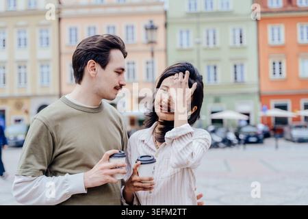 Donna asiatica sorridente al fidanzato mentre tiene un caffè da asporto all'aperto Foto Stock