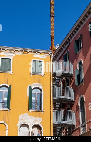 La calda luce del sole illumina le colorate facciate residenziali e una scala antincendio in metallo in un tranquillo quartiere di Venezia, Italia. Foto Stock