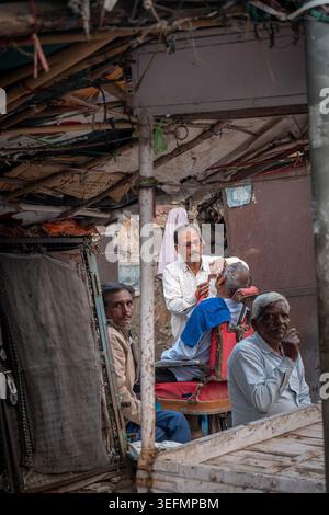 Uomini del luogo in attesa di un taglio di capelli in un mercato di Bundi, India Foto Stock
