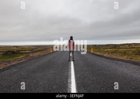Snaefellsness, Islanda - 22 luglio 2016: Un uomo in piedi su una strada nell'Islanda rurale che conduce direttamente all'orizzonte in una nuvolosa giornata estiva. Foto Stock