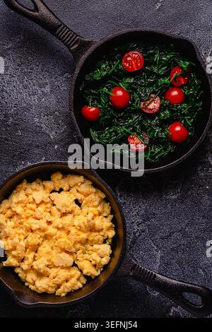 Omelette e spinaci cotti con pomodori in padelle, vista dall'alto. Foto Stock