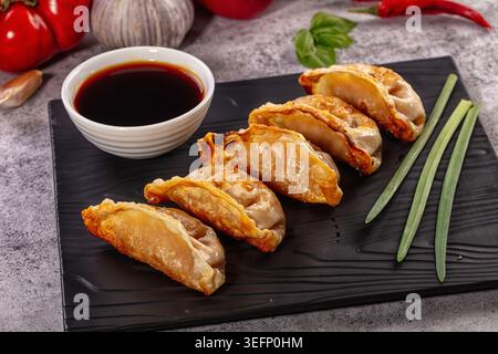 Appetitosi gnocchi fritti in padella asiatici, gyoza, serviti su un piatto scuro con salsa. Ingredienti freschi come aglio e peperoncino sullo sfondo. Chiudere u Foto Stock