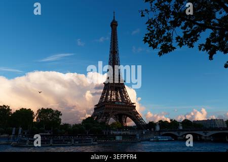 La Torre Eiffel si erge in una sagoma orgogliosa contro un drammatico cielo crepuscolo sopra la Senna, mentre una torreggiante nuvola di cumulus si illumina di rosa e ambra Foto Stock