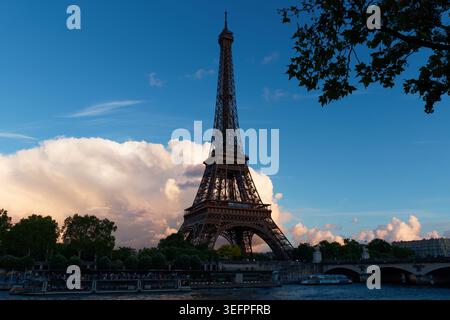 La Torre Eiffel si erge in una sagoma orgogliosa contro un drammatico cielo crepuscolo sopra la Senna, mentre una torreggiante nuvola di cumulus si illumina di rosa e ambra Foto Stock