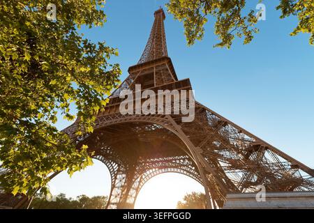 Spettacolare vista a vermi che si affaccia direttamente sull'imponente arco di ferro della Torre Eiffel e sull'imponente struttura a reticolo, incorniciata da un brillante verde estivo Foto Stock
