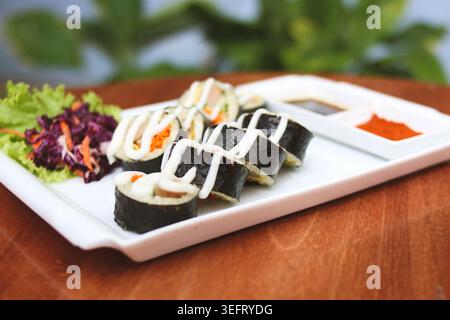 Rotoli di Gimbap in stile coreano con verdure fresche e salsa cremosa serviti su piatto bianco Foto Stock