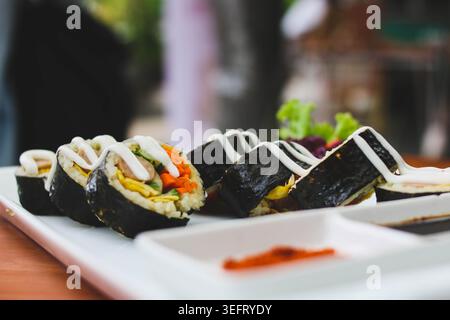 Rotoli di Gimbap in stile coreano con verdure fresche e salsa cremosa serviti su piatto bianco Foto Stock
