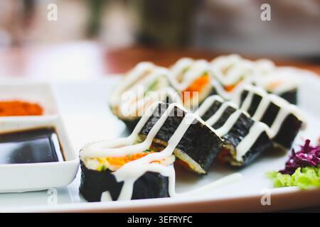 Rotoli di Gimbap in stile coreano con verdure fresche e salsa cremosa serviti su piatto bianco Foto Stock