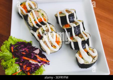 Rotoli di Gimbap in stile coreano con verdure fresche e salsa cremosa serviti su piatto bianco Foto Stock