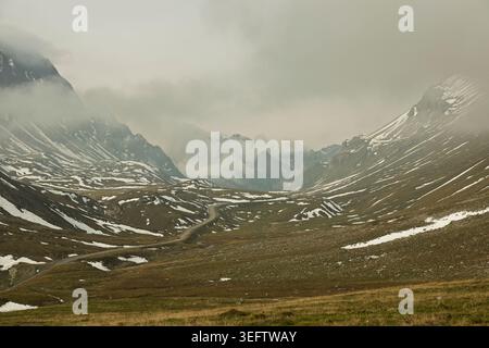 Passo di Albula, Svizzera - 22.09.2024: Una veduta grandangolare di un desolato passo di montagna sotto un pesante cielo coperto. Una strada sterrata si snoda attraverso un alto alt Foto Stock