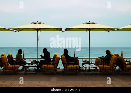 Nizza, Francia 12 aprile 2026 le persone in stile si rilassano in un caffè giallo sulla spiaggia lungo la Promenade des Anglais a Nizza. Idilliaco stile di vita della Costa Azzurra Foto Stock
