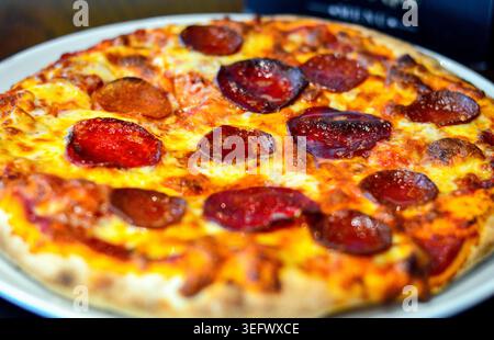 Pizza appena sfornata condita con formaggio e peperoni collocata sul tavolo del ristorante. Foto Stock