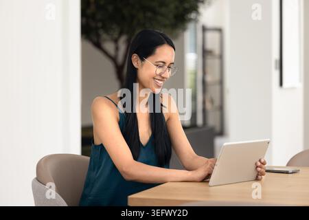 Donna seduta a un tavolo in un accogliente soggiorno con un tablet Foto Stock