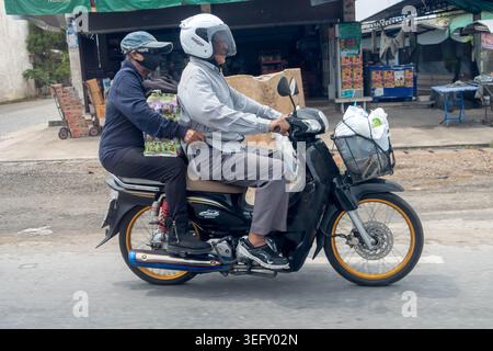 SAMUT PRAKAN, THAILANDIA, 9 MAGGIO 2026, coppia senior in sella a una moto con alimentari in una strada della città di Bangkok Foto Stock