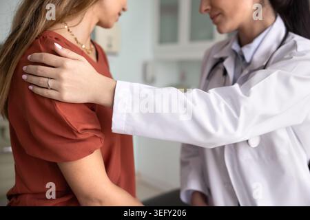 Medico che pone delicatamente la mano sulla spalla della paziente, primo piano Foto Stock