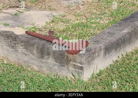 Lapide in ferro arrugginito con numeri in rilievo appoggiato su un marciapiede di cemento in un vecchio cimitero Foto Stock