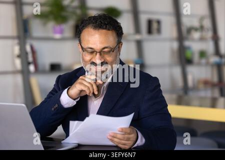 Uomo d'affari di mezza età sorridente che esamina i rapporti finanziari Foto Stock