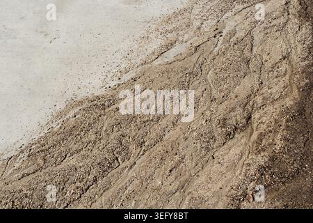 Una struttura di sfondo ad alto angolo che mostra sporco marrone, sabbia e ghiaia fine su una superficie liscia in cemento dopo la pioggia Foto Stock