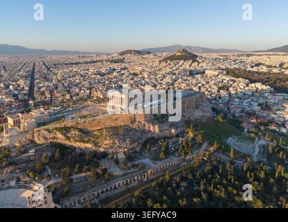 Scatto in droni ad alto angolo del Partenone in cima alla collina dell'Acropoli, che si affaccia sulla vasta estensione urbana di Atene e della collina di Licabetto al tramonto. Foto Stock