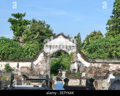 Porta ad arco in pietra intemprata incorniciata da muratura e edera sbriciolate, con alberi lussureggianti e un cielo azzurro limpido, che evocano una calma senza tempo e una serenità storica in un Foto Stock