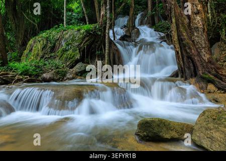 Una cattura verticale di una cascata moltitissima che si getta su rocce muschiate in un fitto ambiente della foresta pluviale tropicale con un effetto acqua fluente. Foto Stock