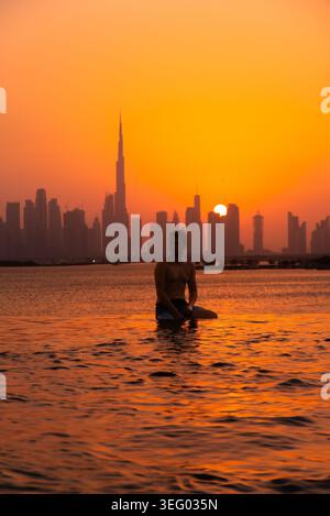 Uomo che si rilassa nella piscina a sfioro con il paesaggio urbano di dubai al tramonto Foto Stock